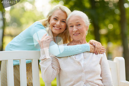 Image of daughter with senior mother hugging on park bench