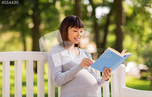 Image of happy pregnant asian woman reading book at park