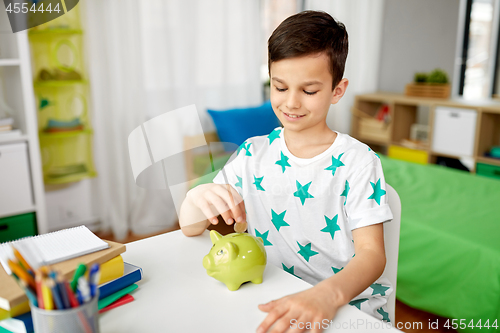 Image of little boy putting coin into piggy bank at home