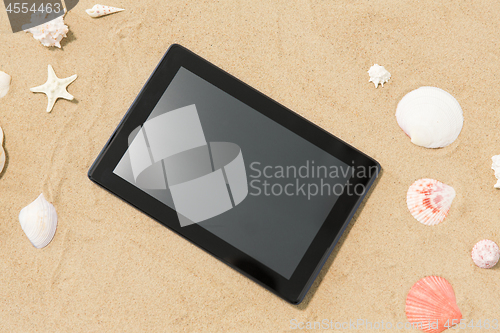 Image of tablet computer and seashells on beach sand