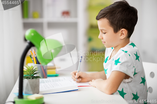 Image of boy with book writing to notebook at home