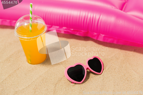 Image of sunglasses, juice and pool mattress on beach sand