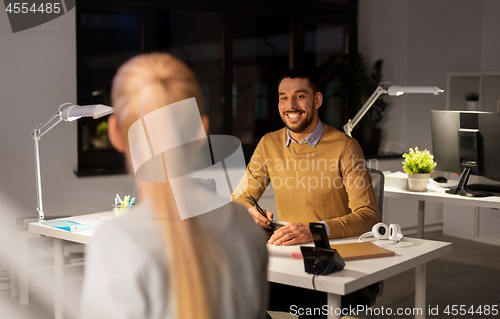 Image of designer with laptop talking to coworker at office