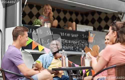 Image of happy friends with drinks eating at food truck