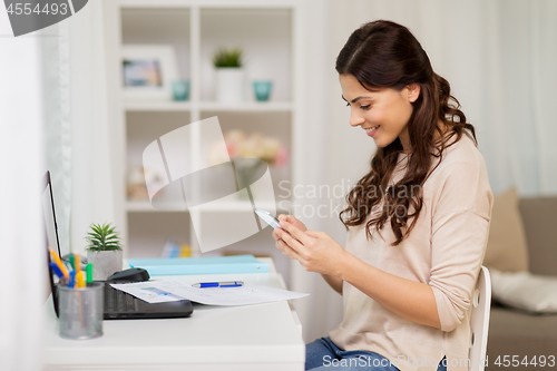 Image of woman with papers and smartphone working at home