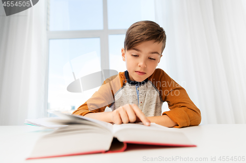 Image of student boy reading book at home table