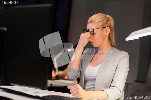 Image of businesswoman rubbing tired eyes at night office