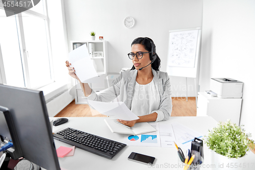 Image of businesswoman with headset and papers at office