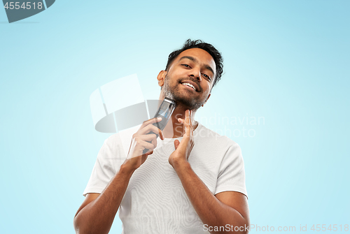 Image of smiling indian man shaving beard with trimmer