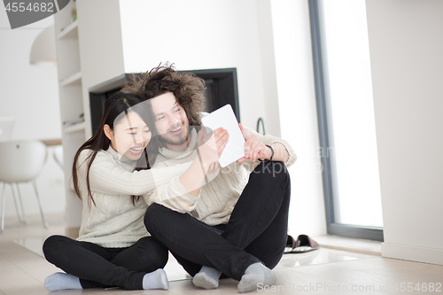 Image of multiethnic couple using tablet computer in front of fireplace