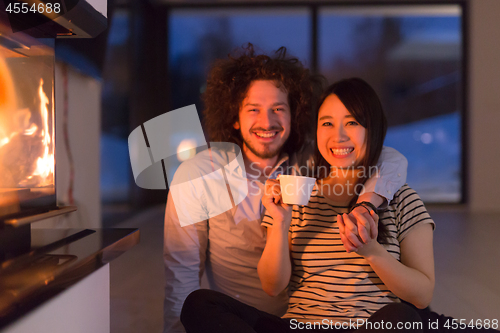 Image of happy multiethnic couple sitting in front of fireplace