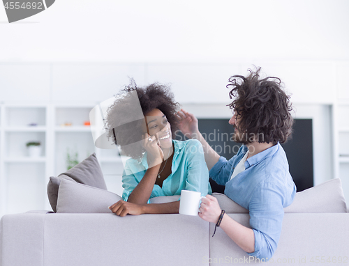 Image of multiethnic couple sitting on sofa at home drinking coffe