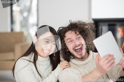 Image of multiethnic couple using tablet computer in front of fireplace