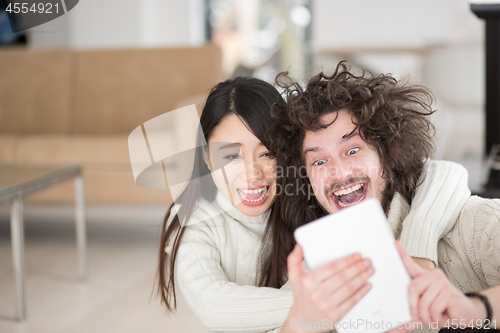 Image of multiethnic couple using tablet computer in front of fireplace