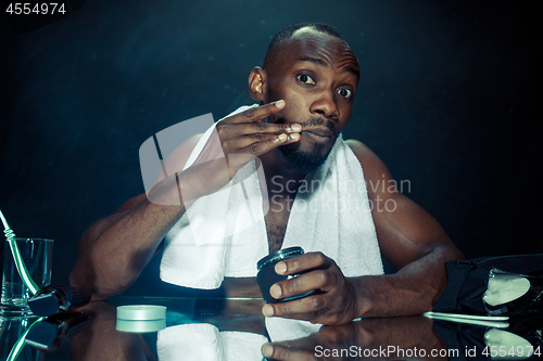 Image of young man in bedroom sitting in front of the mirror after scratching his beard