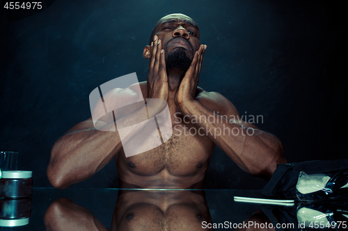 Image of young man in bedroom sitting in front of the mirror after scratching his beard