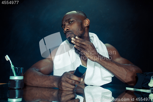 Image of young man in bedroom sitting in front of the mirror scratching his beard