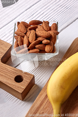 Image of Natural ingredients for healthy breakfast- almonds in a glass bowl and fresh banana on a wooden board on a gray background. Vegetable protein for vegans.