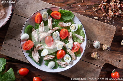 Image of Healthy freshly prepared salad of quail eggs, meat, tomatoes and spinach in a plate on a wooden board on the kitchen table. Dietary lunch. Flat lay