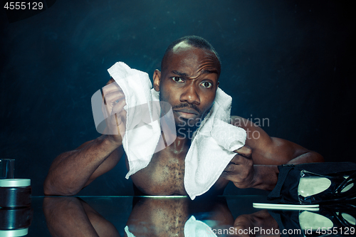 Image of young man in bedroom sitting in front of the mirror after scratching his beard