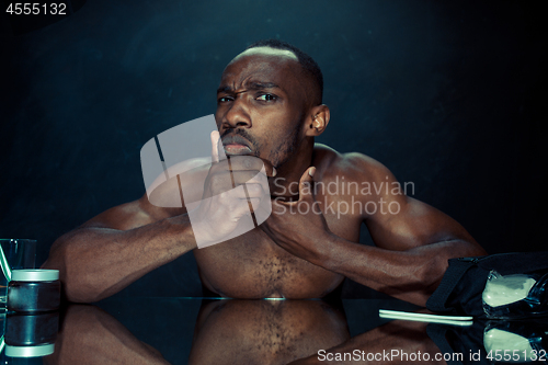 Image of young man in bedroom sitting in front of the mirror after scratching his beard