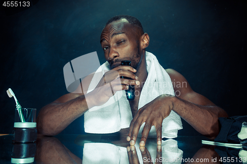 Image of young man in bedroom sitting in front of the mirror scratching his beard