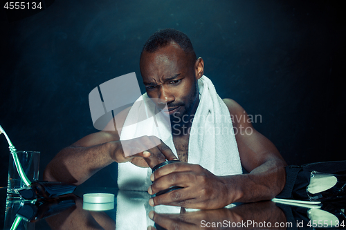 Image of young man in bedroom sitting in front of the mirror after scratching his beard