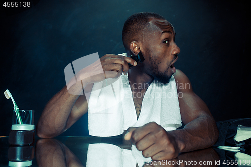 Image of young man in bedroom sitting in front of the mirror scratching his beard