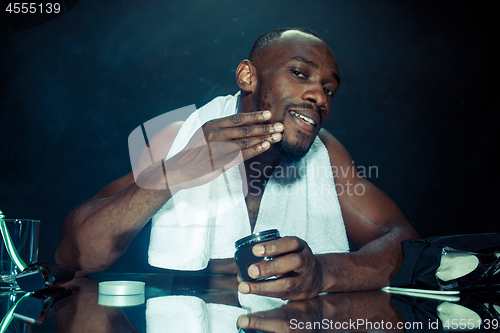 Image of young man in bedroom sitting in front of the mirror after scratching his beard