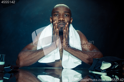 Image of young man in bedroom sitting in front of the mirror after scratching his beard