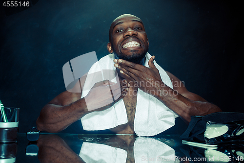 Image of young man in bedroom sitting in front of the mirror after scratching his beard