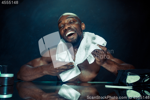 Image of young man in bedroom sitting in front of the mirror after scratching his beard