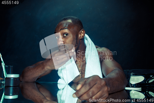 Image of young man in bedroom sitting in front of the mirror after scratching his beard