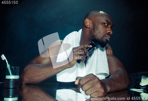 Image of young man in bedroom sitting in front of the mirror scratching his beard