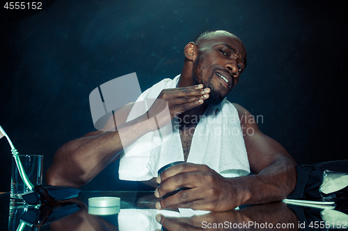 Image of young man in bedroom sitting in front of the mirror after scratching his beard