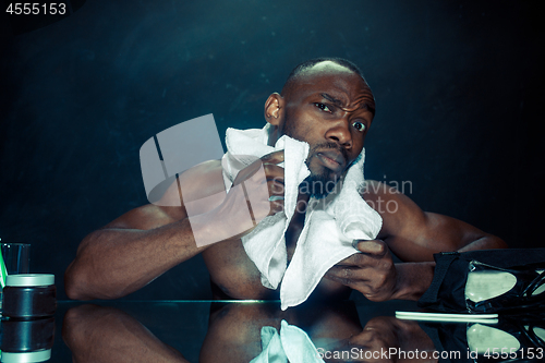 Image of young man in bedroom sitting in front of the mirror after scratching his beard