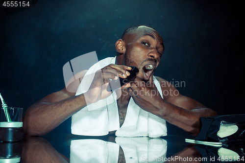 Image of young man in bedroom sitting in front of the mirror scratching his beard