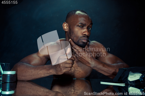 Image of young man in bedroom sitting in front of the mirror after scratching his beard