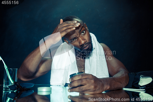 Image of young man in bedroom sitting in front of the mirror after scratching his beard