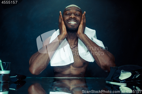 Image of young man in bedroom sitting in front of the mirror after scratching his beard