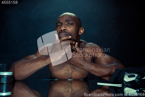 Image of young man in bedroom sitting in front of the mirror after scratching his beard