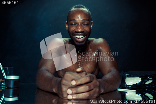 Image of young man in bedroom sitting in front of the mirror after scratching his beard