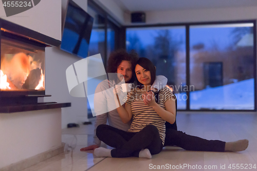 Image of happy multiethnic couple sitting in front of fireplace