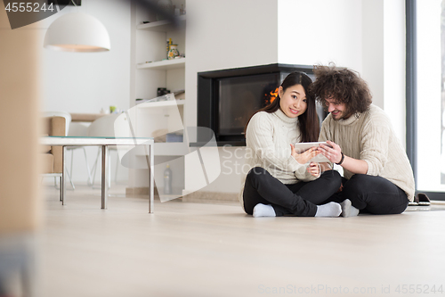 Image of multiethnic couple using tablet computer in front of fireplace