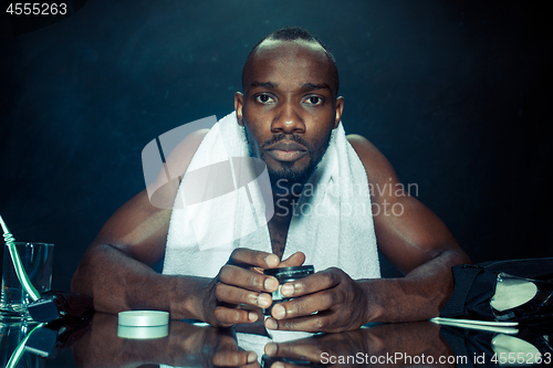 Image of young man in bedroom sitting in front of the mirror after scratching his beard