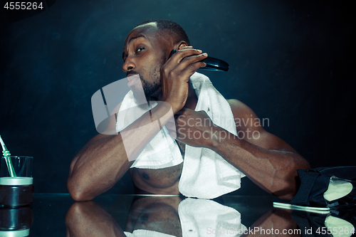 Image of young man in bedroom sitting in front of the mirror scratching his beard