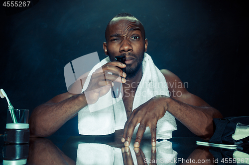 Image of young man in bedroom sitting in front of the mirror scratching his beard