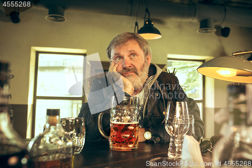 Image of The sad senior bearded male drinking beer in pub