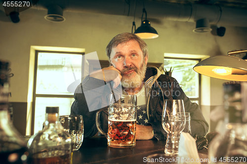 Image of The sad senior bearded male drinking beer in pub