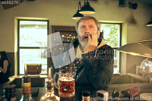 Image of The sad senior bearded male drinking beer in pub